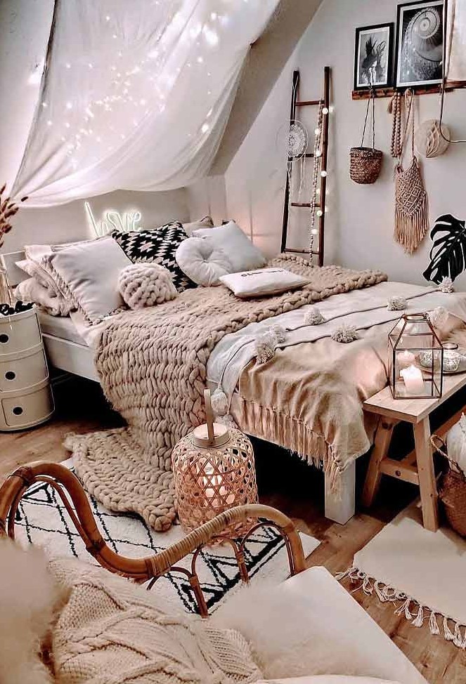 a neutral boho bedroom with layered bedding, a shelf gallery wall, a canopy with lights, candle lanterns and a rattan chair
