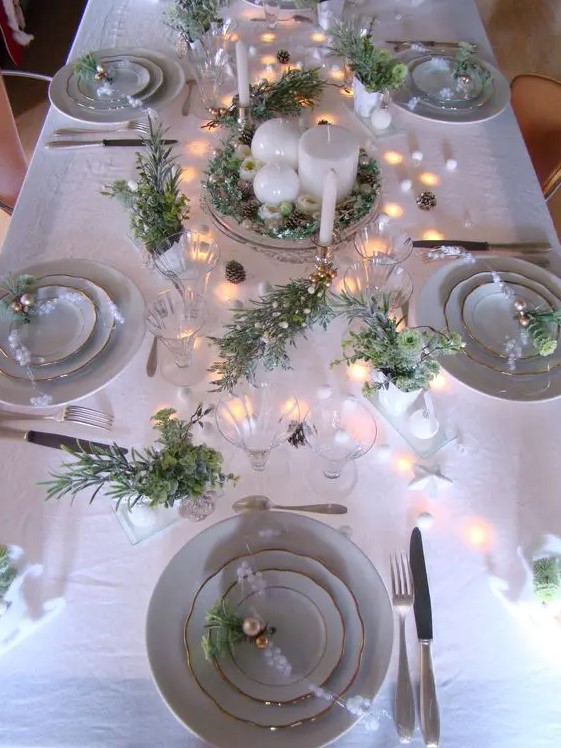 a neutral holiday table setting with lots of fresh greenery, ornaments, lights and candles