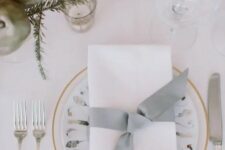 a neutral tablescape with metallic ornaments, evergreens, candles and printed plates