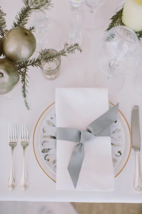 a neutral tablescape with metallic ornaments, evergreens, candles and printed plates