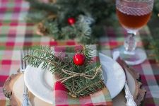 a plaid tablecloth, plaid napkins and evergreens with berries for a cozy rustic tablescape will create a festive feel at your Christmas table