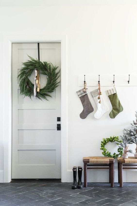 a pretty Christmas entryway with an evergreen wreath, a rack with matching stockings of various colors and mini Christmas trees