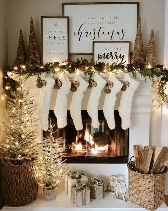 a pretty and shiny Christmas mantel with an evergreen and light garland, yarn Christmas trees, signs, dried fruit slices, white stockings