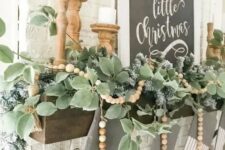 a pretty farmhouse Christmas mantel with a greenery garland and wooden beads, candles in wooden candleholders and striped stockings plus a black and white sign