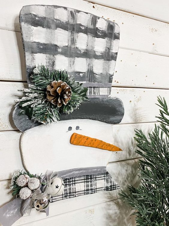 a pretty snowman decoration with a plaid scarf and a plaid top hat, with evergreens and a pinecone is a lovely decor idea for Christmas