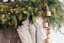 a pretty woodland or cabin mantel with an evergreen and light garland, vintage bells and white knit stockings for Christmas