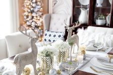 a refined Christmas tablescape in white spruced up with gold ornaments, cutlery, candleholders and glitter deer figurines
