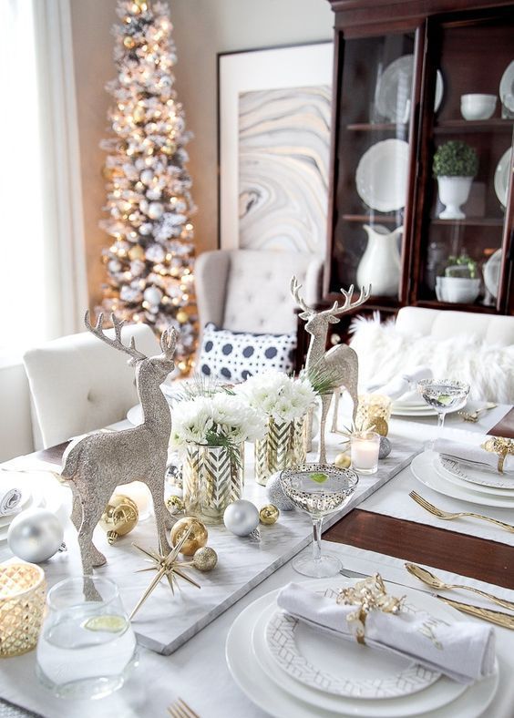 a refined Christmas tablescape in white spruced up with gold ornaments, cutlery, candleholders and glitter deer figurines