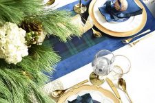 a refined Christmas tablescape with dark plaid linens, gold chargers and cutlery and neutral blooms and evergreens