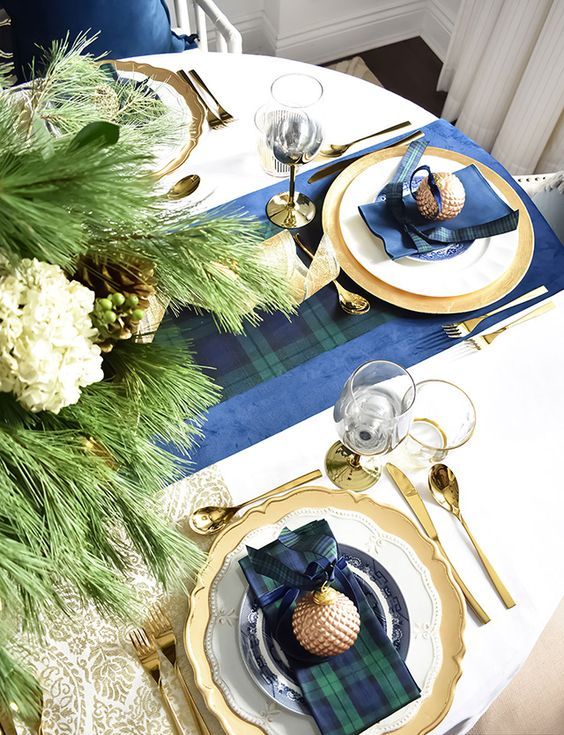 a refined Christmas tablescape with dark plaid linens, gold chargers and cutlery and neutral blooms and evergreens