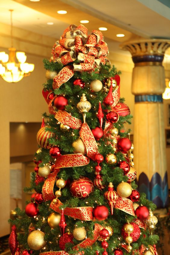 a refined red and gold Christmas tree with a large bow on top, lots of ornaments and lights