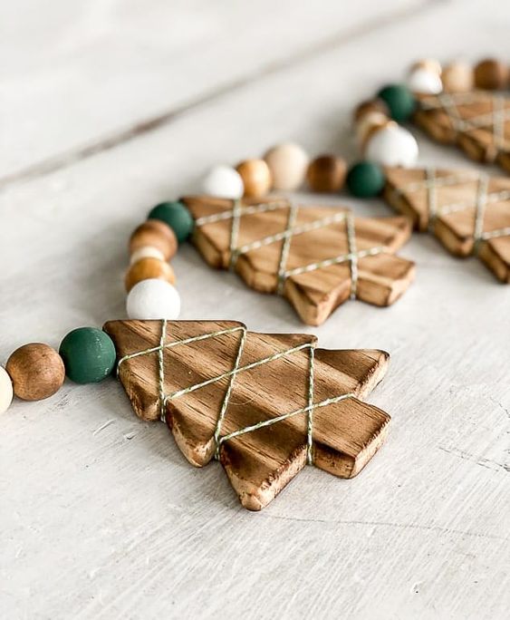 a rustic Christmas garland of wooden Christmas trees with twine, white, stained and green wooden beads is a pretty idea