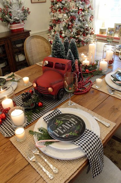 a rustic retro Christmas tablescape with a buffalo check runner and napkins, woven placemats, a red truck with bottle brush Christmas trees and candles