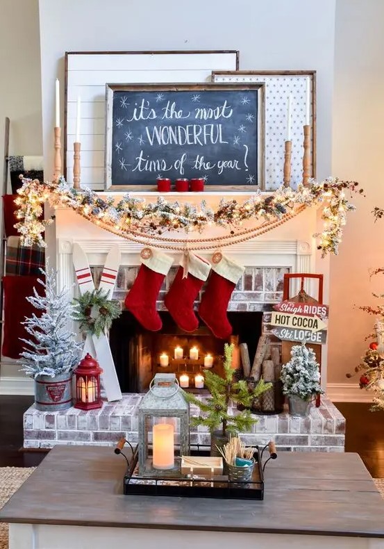 a ski lodge Christmas mantel with a snowy evergreen garland with red berries, a pompom garland, red stockings and mismatching signs