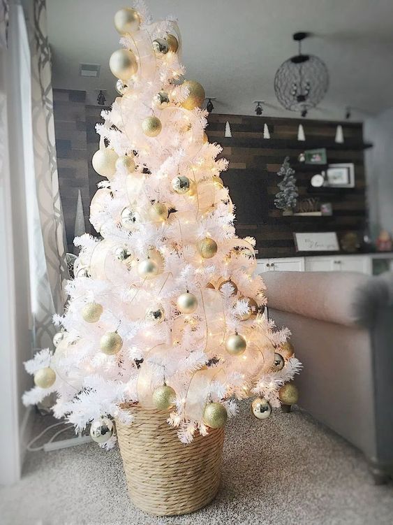 a small white christmas tree with lights and gold and pearly ornaments placed into a basket is cool