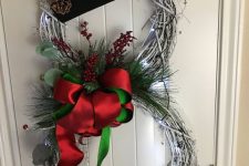 a snowman door decoration of white vine wreaths, green and red ribbons, a top hat and pinecones is a pretty idea to rock