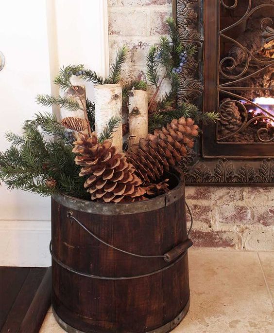 دلو خشبي ملطخ مع أكواز صنوبر كبيرة الحجم ، وحطب ، وخضرة دائمة ، هو زخرفة ريفية جميلة لعيد الميلاد على الصخور