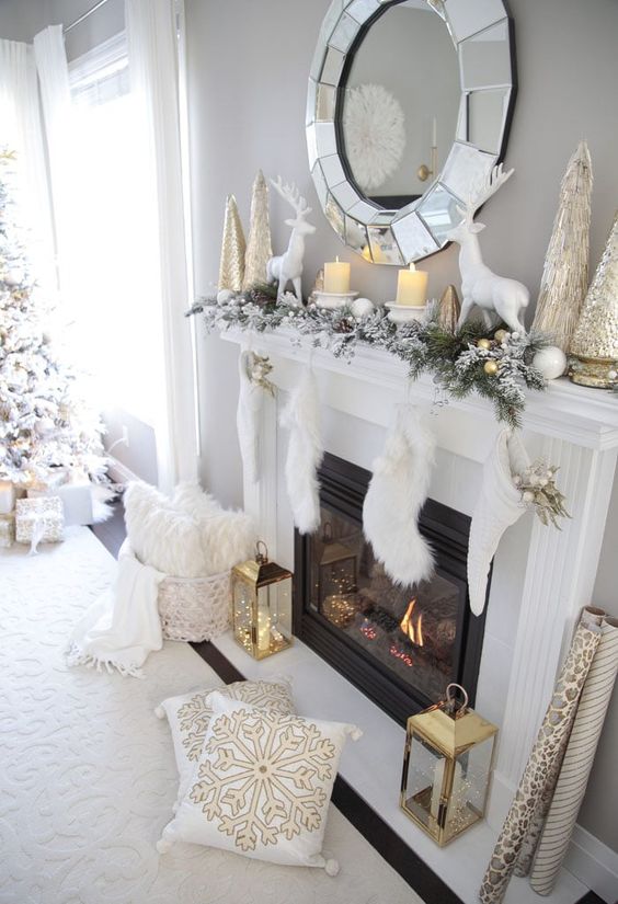 a super refined gold and white Christmas mantel with gilded Christmas mini trees and candleholders, white deer, large metlalic trees and white stockings with gold leaves