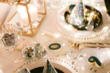 a super shiny NYE party tablescape in gold and white, with stacked candleholders, white plates and clear chargers, gold cutlery and disco balls