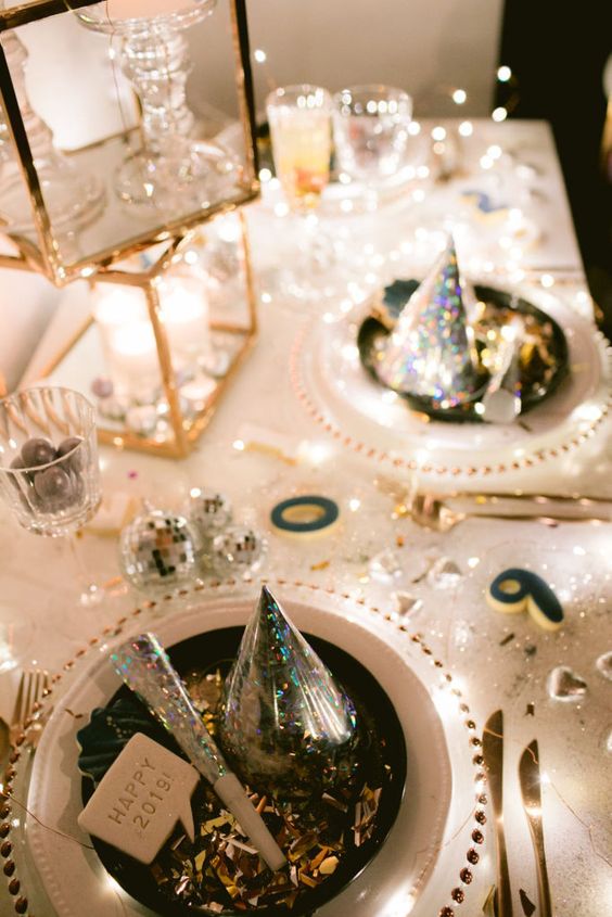 a super shiny NYE party tablescape in gold and white, with stacked candleholders, white plates and clear chargers, gold cutlery and disco balls
