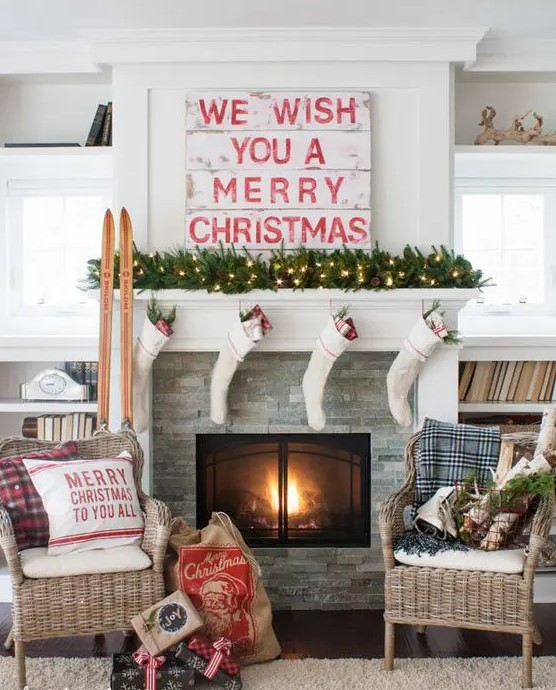 a traditional Christmas mantel with a light evergreen garland, white stockings, a sign, skis and some plaid touches here and there