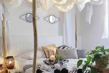 a tropical-inspired bedroom wih a pallet and branch bed, black and white bedding, potted greenery, candle lanterns and curtains with lights over the bed