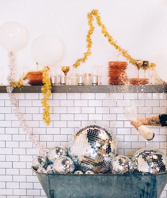 a vintage bathtub filled with disco balls and gold tinsel garlands used for NYE decor are amazing