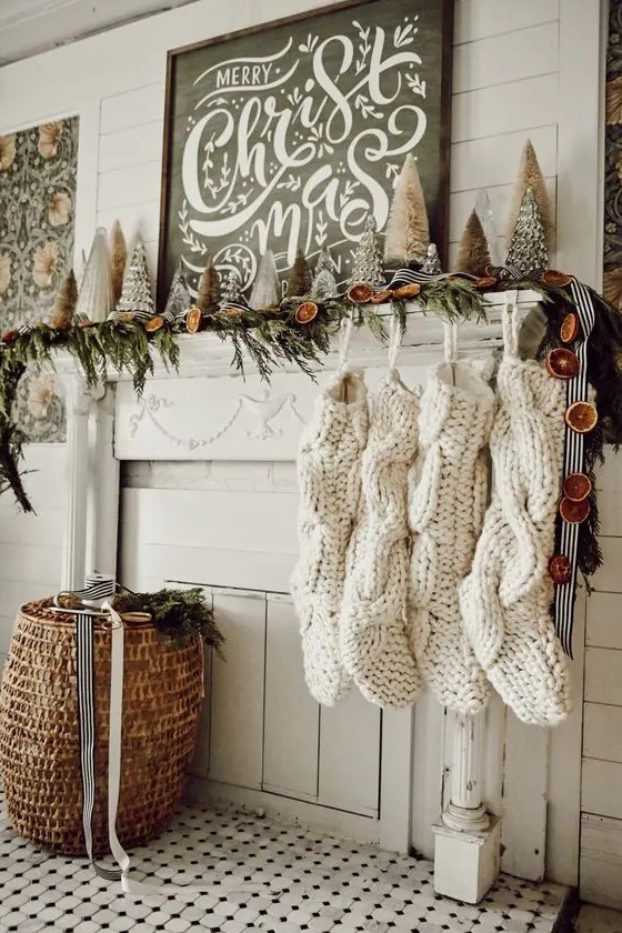 a whimsy Christmas mantel with an evergreen and dried fruit slice garland, mini Christmas trees and oversized white stockings