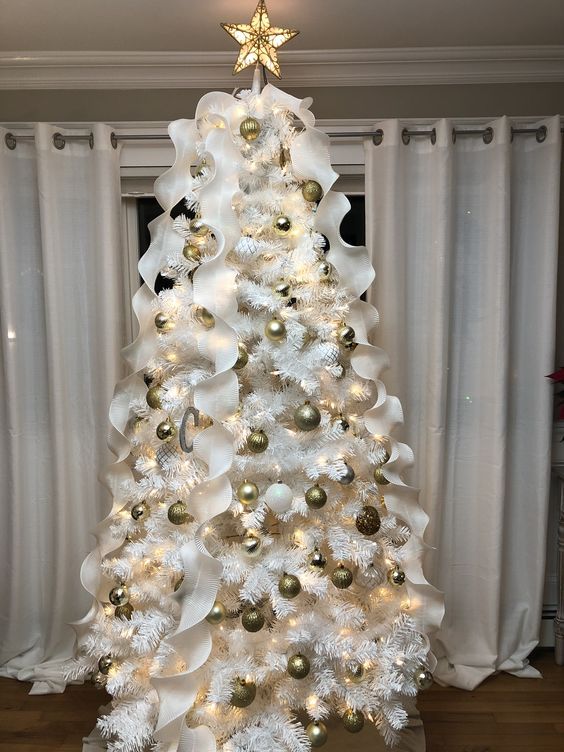 a white Christmas tree with gold and white ornaments, white ruffle ribbons and a lit up tree topper