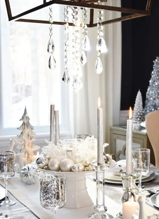 a white and silver table setting with pearly and silver ornaments, a crystal chandelier and patterned glasses