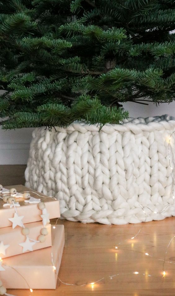 a white chunky knit cover for the tree base is a very creative and cool-looking idea to hide an eye-sore and make your tree more holiday-like