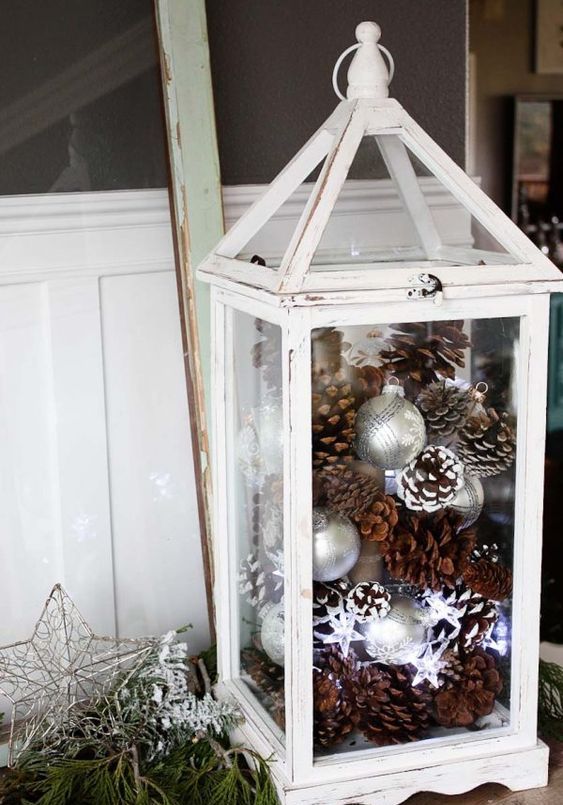 a white lantern with silver ornaments and usual and snowy pinecones is a gorgeous indoor or outdoor decoration for Christmas