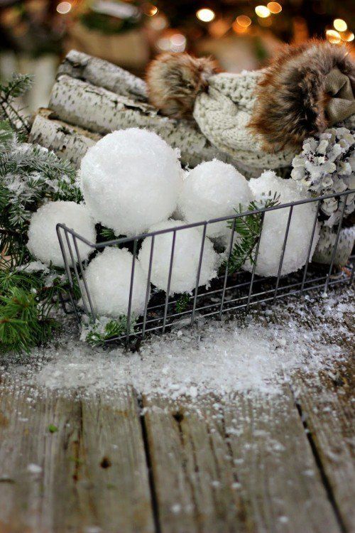 a wire basket with shiny snowballs, fir twigs, firewood, snowy pinecones and a cable knit beanie is a very cozy decoration