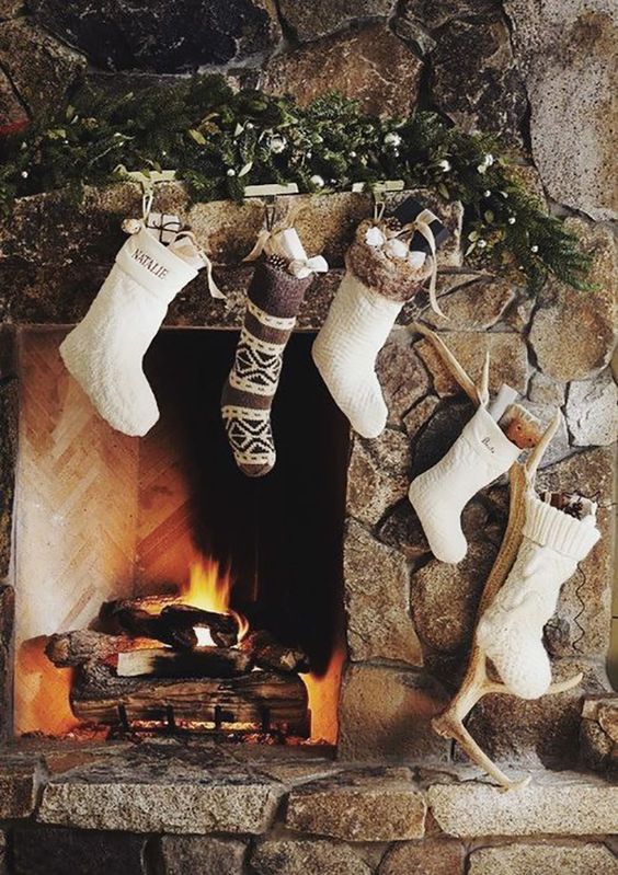 a woodland hearth with white and brown knit stockings, antlers, pinecones, evergreens and ornaments is a very cozy nook