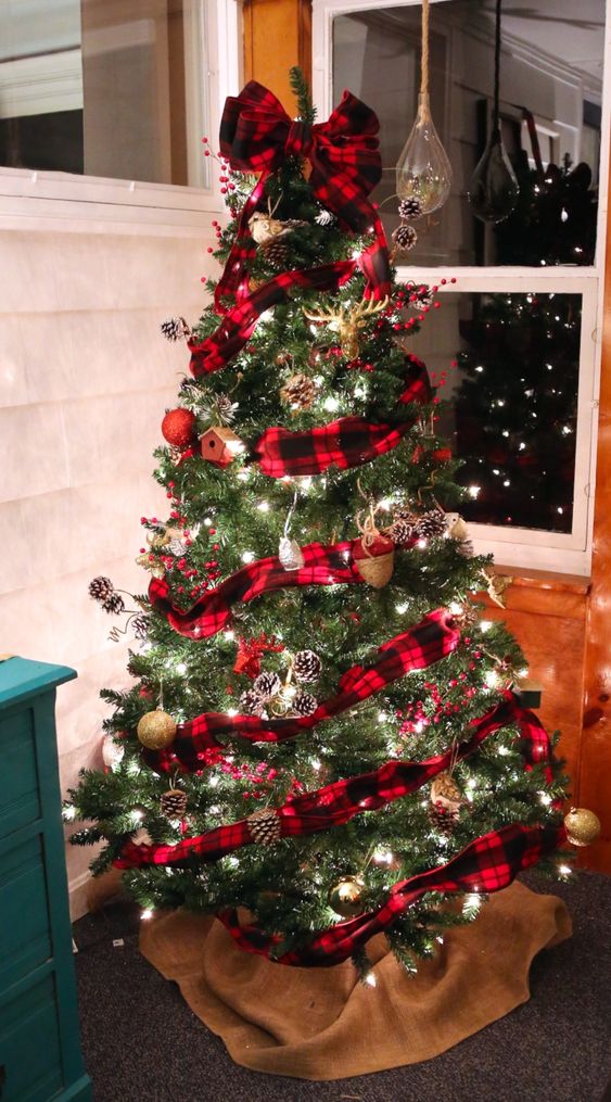 an amazing woodland Christmas tree with a red plaid ribbon, snowy pinecones, lights and red and gold glitter ornaments