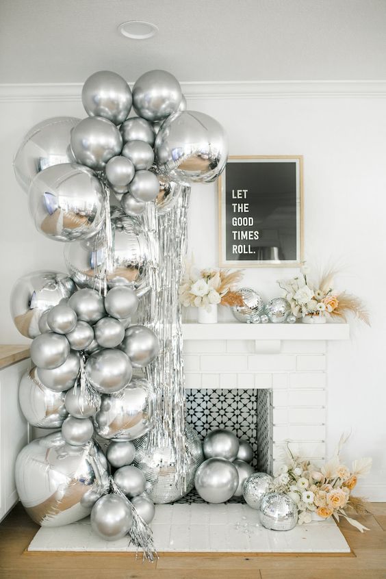 an arrangement of silver balloons next to the fireplace and in it, neutral florals and disco balls on the mantel for a NYE party
