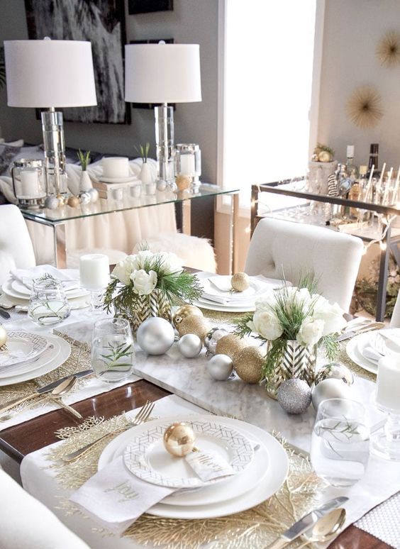 an elegant Christmas tablescape with gold leaf chargers, gold and silver ornaments, white blooms in chevron vases and white candles