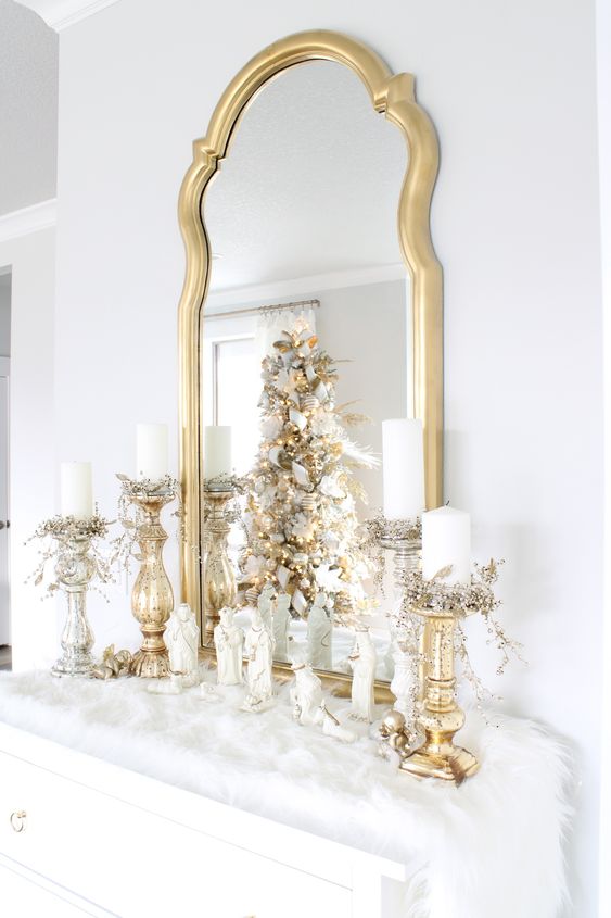 an elegant gold and white Christmas mantel covered with faux fur, with gold candleholders, candles and a mirror in a gold frame