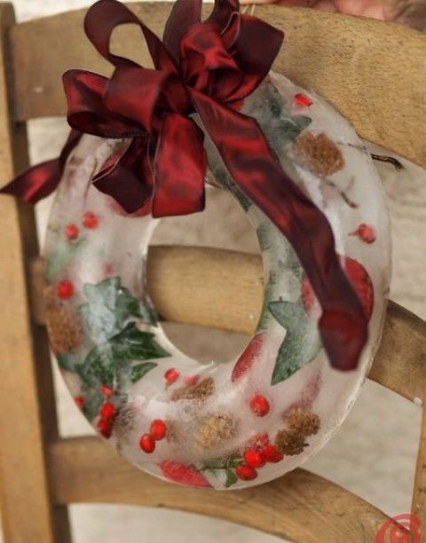 an ice Christmas wreath showing off some cranberries, leaves and pinecones and a burgundy bow on top