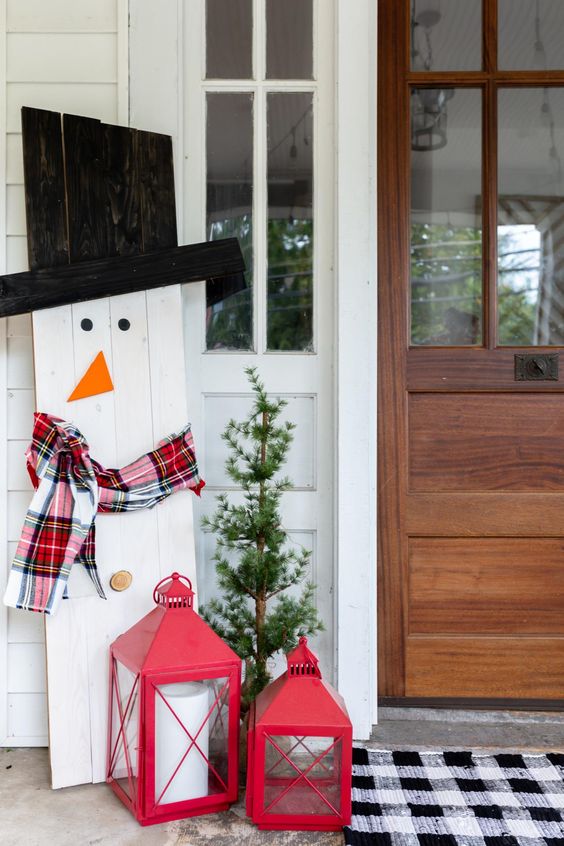 cozy and simple Christmas outdoor decor with a plywood snowman in a plaid scarf, with a top hat and red candle lanterns