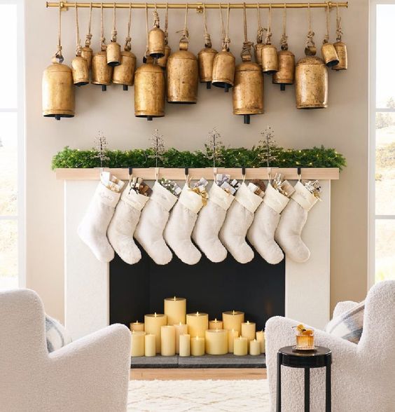 lovely Christmas decor with oversized gold and brass bells, white stockings, an evergreen garland with lights and pillar candles