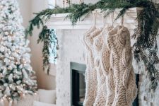 oversized white braided stockings and evergreens make the mantel look very cozy and holiday-like, and tall and thin candles add elegance