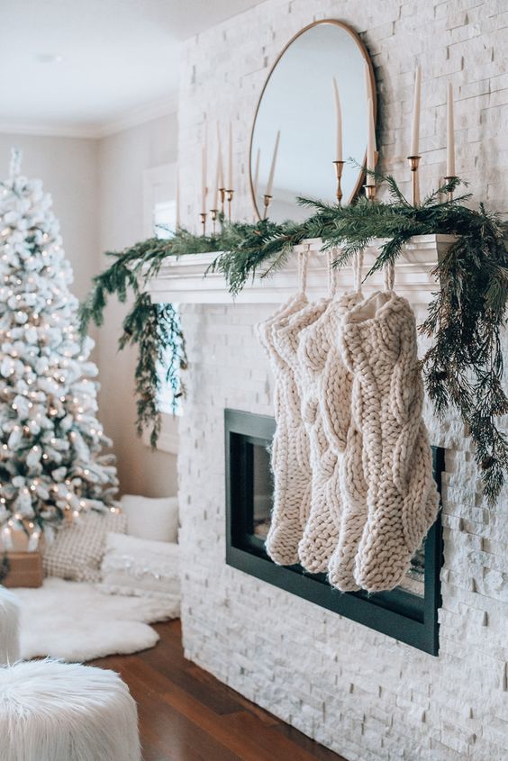 oversized white braided stockings and evergreens make the mantel look very cozy and holiday like, and tall and thin candles add elegance