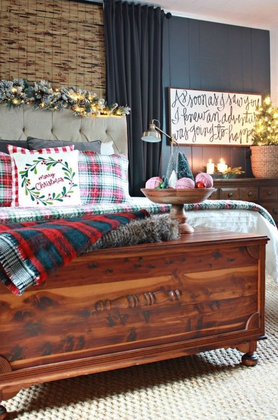 plaid bedding, a snowy evergreen and lights garland, a calligraphy sign, candles, a mini tree in a basket and a bowl with yarn balls and mini trees