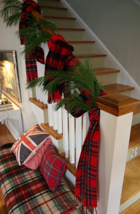 pretty Christmas decor with evergreens and plaid scarves on the railing, a plaid bench with plaid pillows is very cozy
