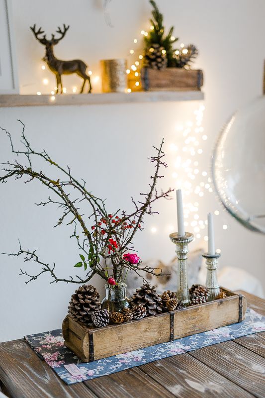rustic Christmas decor with a wooden box with pinecones, candles, branches and berries, a crate with pinecones and a deer on the shelf