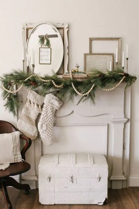 a beautiful vintage Christmas mantel with an evergreen and pinecone garland, a pompom one, vintage frame pictures and candles