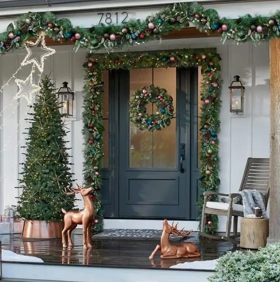 a bold Christmas porch with evergreen garlands with bold ornaments, copper deer, a Christmas tree with lights and star lights over the space