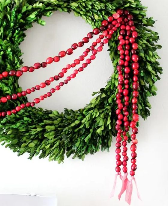 a boxwood Christmas wreath with cranberry garlands is a very cool and bold decor idea for the holidays