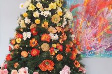 a bright ombre Christmas tree decorated with faux flowers and topped with bold faux sunflowers and blooming branches